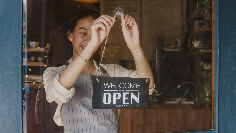 young manager girl changing sign from closed open sign door cafe looking outside waiting clients after lockdown